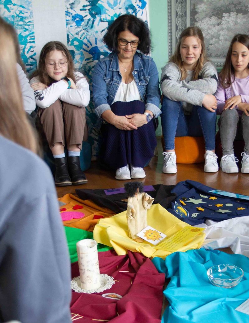 Schülerinnen und eine Lehrkraft im Kreis um ein Bodenbild mit Kerze, Maria-Ward-Realschule Neuburg
